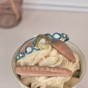 Bracelet fleur de vie et pierre de lune posé sur une tasse de crème dessert avec des biscuits, ton pastel.